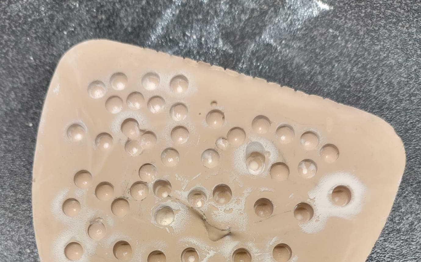 Class III dental stone test specimen after accelerated drill-wear challenge, showing dozens of osteotomy cavities cut into the surface at controlled intervals.