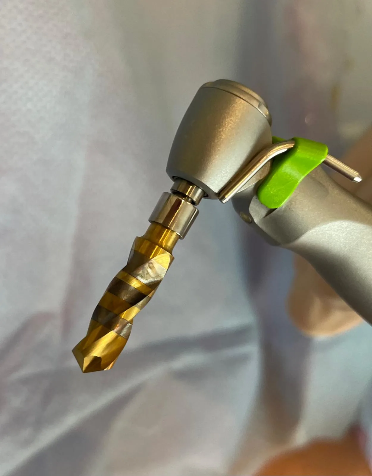 Close-up of a fresh Crown Down tungsten carbide implant drill with titanium-nitride coating mounted on the surgical handpiece before the osteotomy
