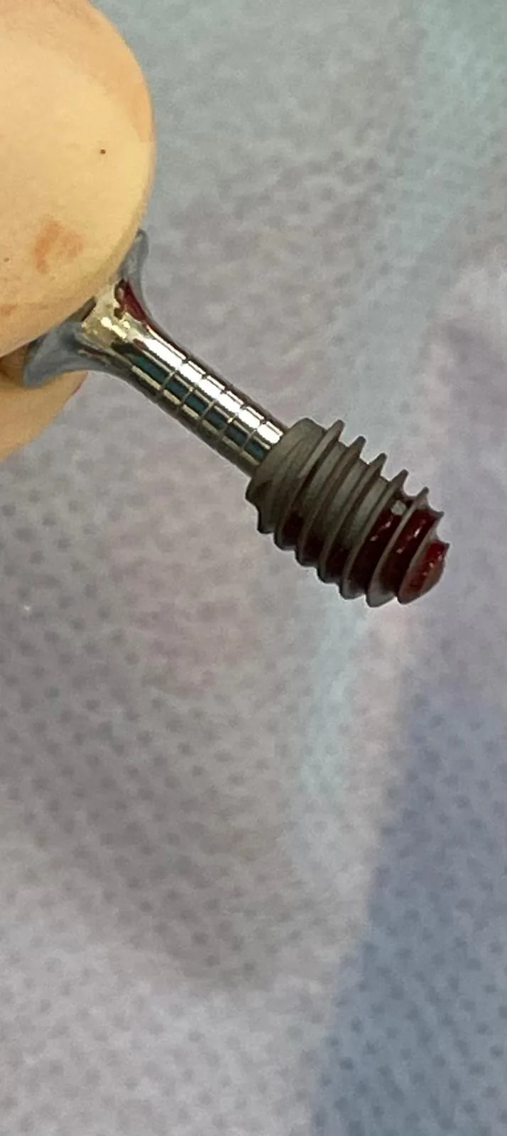 Close-up of a dental implant mounted on the delivery driver against a neutral surgical background, ready for seating