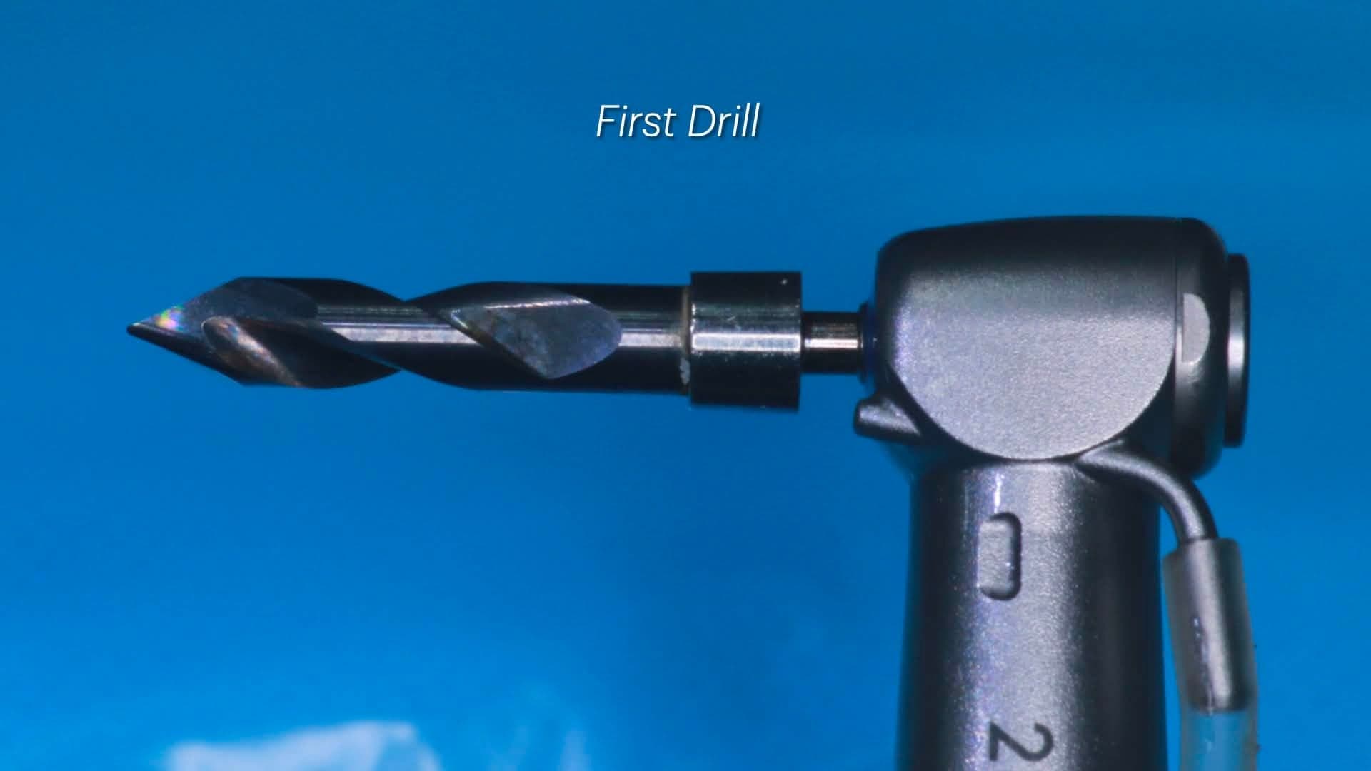 Close-up of the Crown Down cortical carbide drill mounted on the surgical handpiece against a blue photographic backdrop